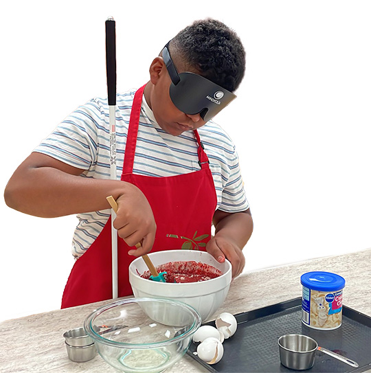 An NFB BELL student mixes cookie batter under sleepshades during cooking class.